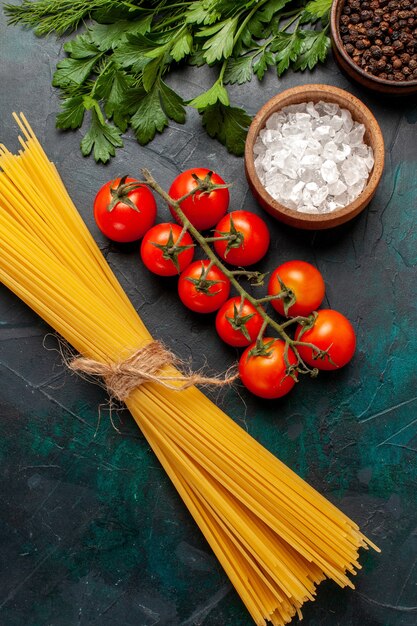 Pasta italiana cruda vista dall'alto con condimenti e pomodori rossi su ingrediente crudo di farina di cibo superficie scura