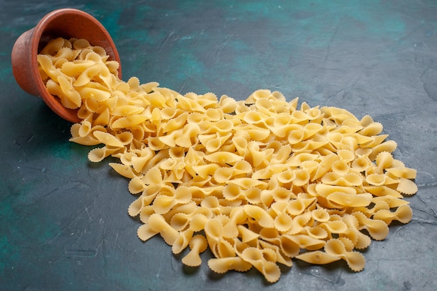 Pasta italiana di pasta cruda gialla vista frontale all'interno della pentola marrone sulla superficie blu scuro