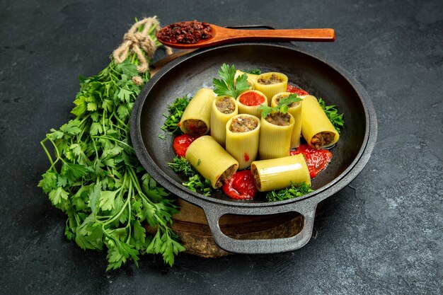 Pasta italiana vista frontale con salsa di pomodoro verde e carne all'interno della padella su uno spazio grigio