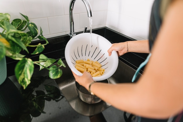 Pasta rigatoni di lavaggio a mano della donna nella colapasta bianca