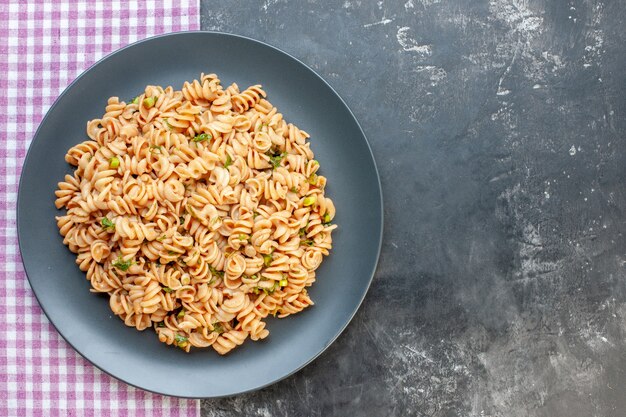 Pasta rotini vista dall'alto su piatto rotondo su tovaglia a quadretti rosa bianca su superficie scura con spazio libero