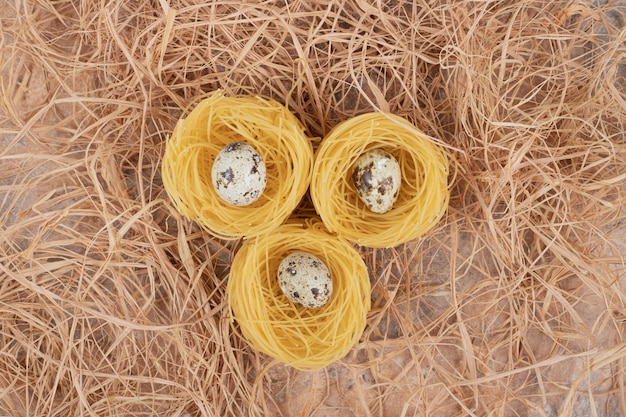 Pasta rotonda cruda con uova di quaglia su spazio di marmo.