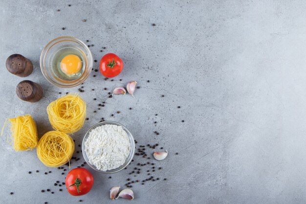 Pasta secca cruda del nido con uova crude e verdure su uno sfondo di pietra.