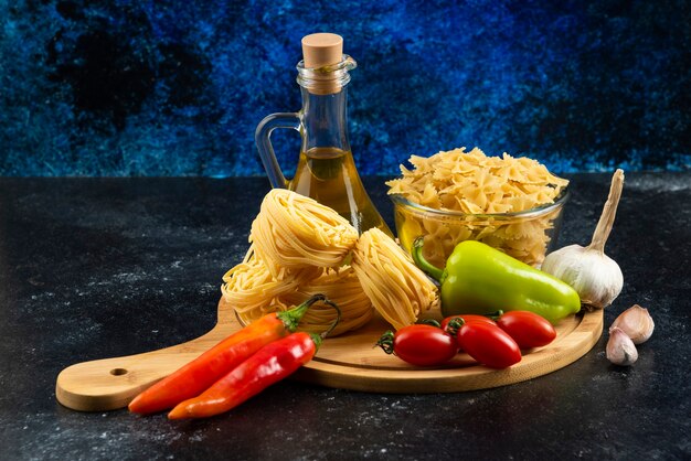 Pasta secca, olio e verdure su tavola di legno.