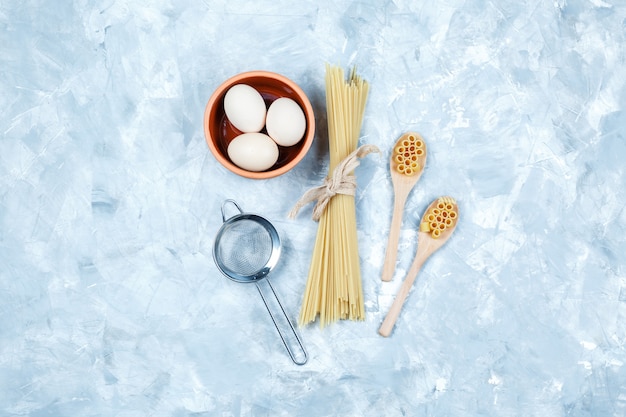 Pasta vista dall'alto in cucchiai di legno con uova, colino su sfondo grigio sgangherato. orizzontale