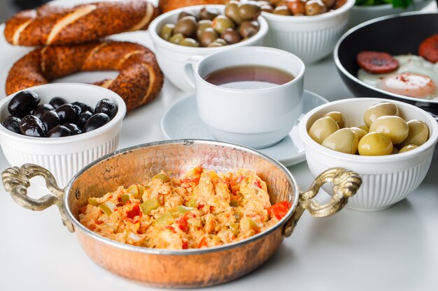 Pasti deliziosi di vista dell'angolo alto in vaso con una tazza di tè, bagel turco, pomodori, verdi su superficie bianca