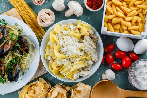 Pasti di pasta in piatti con pasta cruda, pomodoro, farina, funghi, uova, spezie, cucchiaio