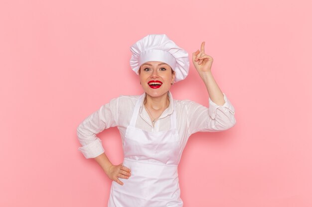 Pasticcere femminile di vista frontale nell'usura bianca che posa con l'espressione felice sul lavoro di lavoro di pasticceria dolce della pasticceria della parete rosa-chiaro