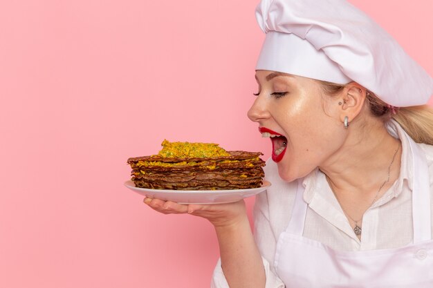 Pasticcere femminile di vista frontale nell'usura bianca che tiene i pasticcini deliziosi sulla pasticceria dolce della pasticceria del pavimento rosa