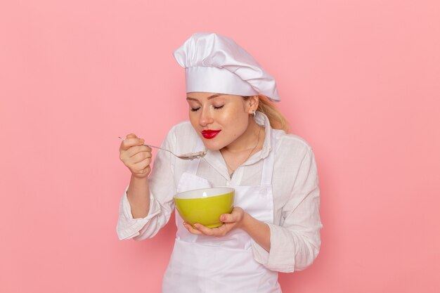 Pasticcere femminile di vista frontale nell'usura bianca che tiene il piatto verde con la colomba che lo assaggia sulla zuppa di cena di verdure verdi del pasto del cibo della parete rosa