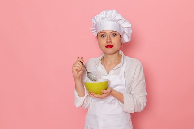 Pasticcere femminile di vista frontale nell'usura bianca che tiene il piatto verde con la colomba che lo assaggia sulla zuppa di cena di verdure verdi del pasto dello scrittorio rosa