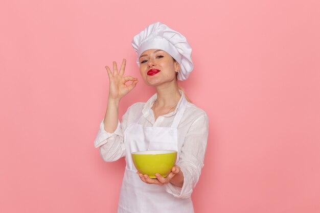 Pasticcere femminile di vista frontale nell'usura bianca che tiene il piatto verde con la colomba sulla zuppa di cena di verdure verdi del pasto del cibo della parete rosa