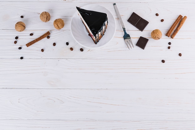 Pasticcino; Noci; cannella; chicchi di caffè; forchetta e barretta di cioccolato su sfondo bianco in legno