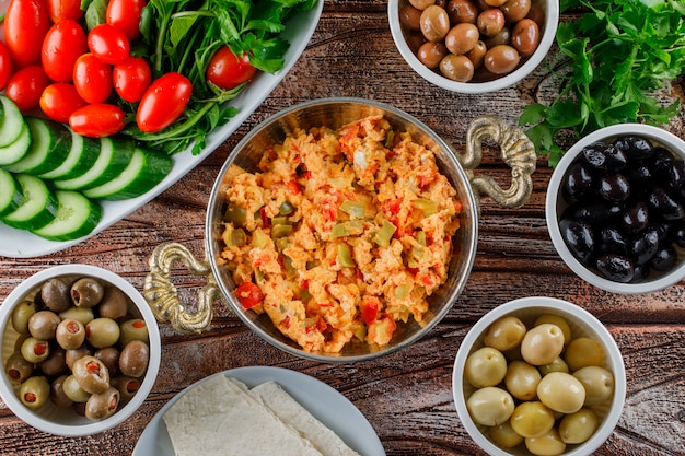 Pasto delizioso di vista superiore in vaso con insalata, sottaceti in ciotole su superficie di legno