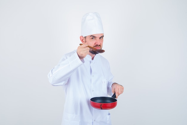 Pasto di degustazione di giovane chef maschio con cucchiaio di legno in uniforme bianca e curioso, vista frontale