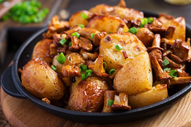 Patate al forno con aglio, erbe e finferli fritti in una padella di ghisa.