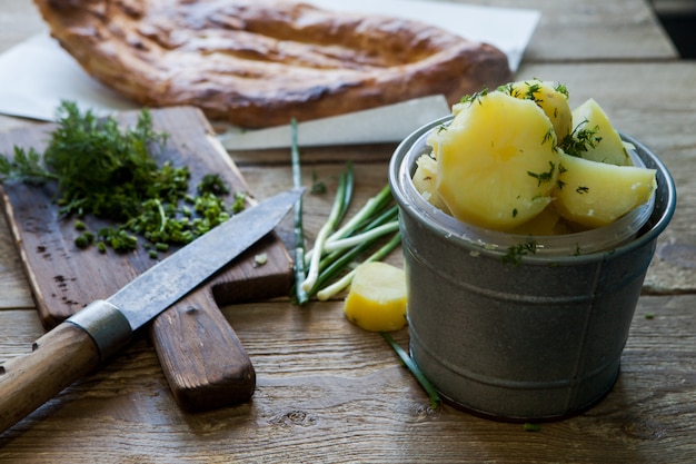 Patate bollite vista laterale con le cipolle verdi e pane e coltello in tavola sulla tavola di legno