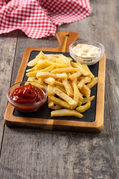 Patate fritte con ketchup e maionese su tavola di legno