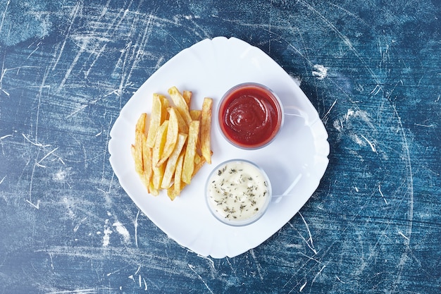 Patate fritte con salse in un piatto bianco.