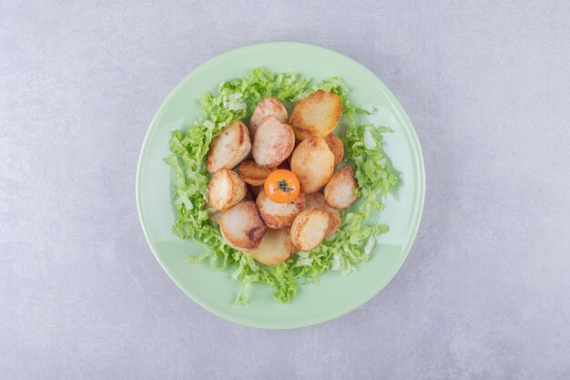 Patate fritte e lattuga sul piatto verde.