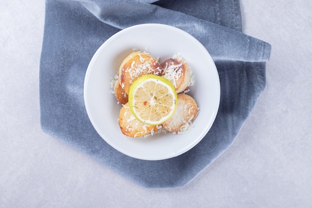 Patate fritte guarnite con formaggio grattugiato e limone sul piatto bianco.