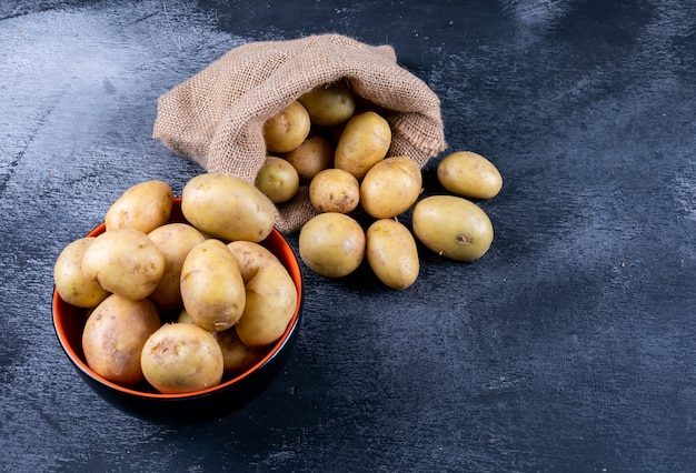 Patate in un sacchetto di sacco e ciotola su un tavolo scuro