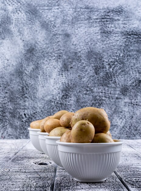 Patate in una vista laterale di ciotole su un tavolo di legno grigio