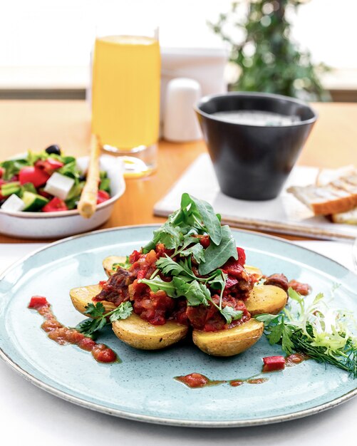 Patate vista frontale con carne in salsa di pomodoro con rucola e insalata greca sul tavolo