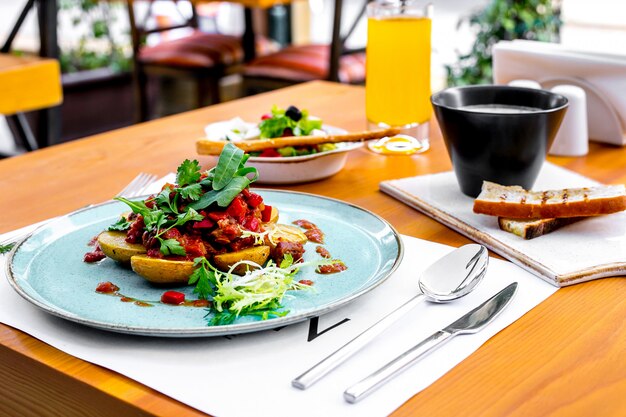 Patate vista laterale con carne in salsa di pomodoro con rucola e insalata greca e zuppa sul tavolo