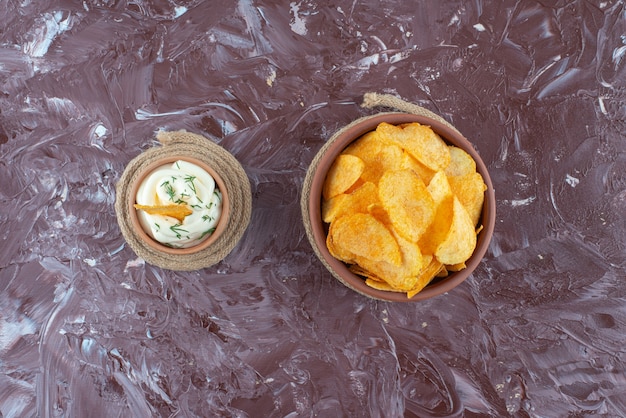 Patatine croccanti e yogurt in piatti su sottopentola, sul tavolo di marmo.