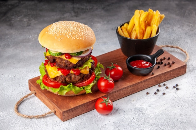 Patatine fritte del pepe del ketchup dei pomodori del panino fatto in casa sul tagliere di legno su superficie vaga