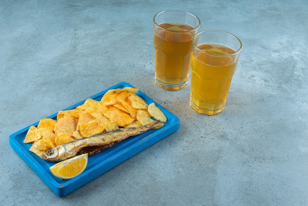 Patatine fritte e pesce su un piatto di legno accanto a due bicchieri di birra, sul tavolo di marmo.