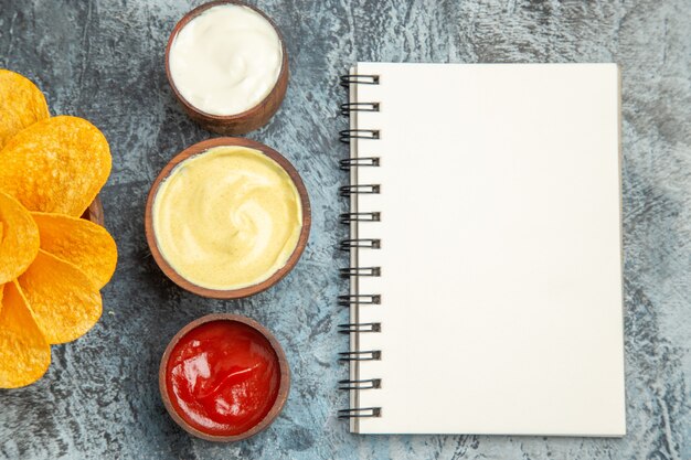 Patatine fritte fatte in casa decorate come un fiore a forma di e sale con maionese ketchup e taccuino sul tavolo grigio