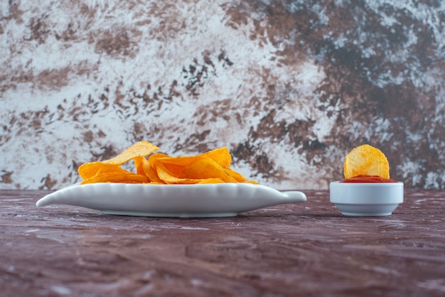 Patatine fritte in un piatto accanto al ketchup in una ciotola, sul tavolo di marmo.