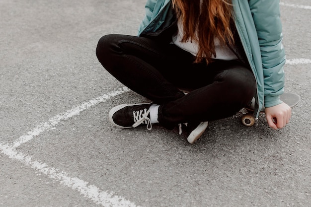 Pattinatore femminile che si siede accanto al suo skateboard all'aperto