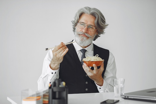 Pausa pranzo. Uomo elegante in ufficio. Uomo d'affari in camicia bianca. L'uomo mangia le tagliatelle.