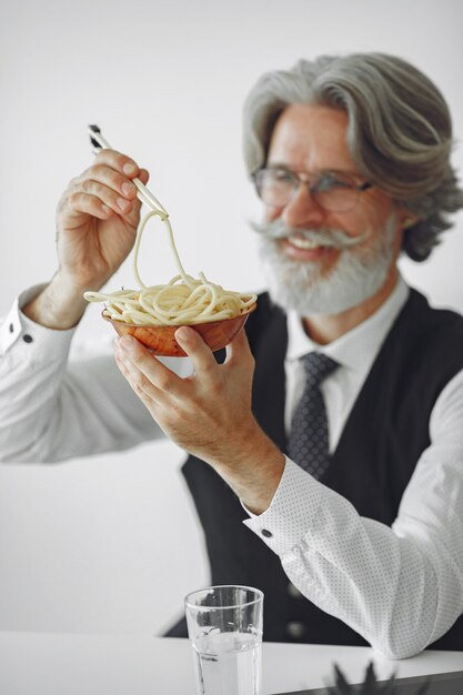 Pausa pranzo. Uomo elegante in ufficio. Uomo d'affari in camicia bianca. L'uomo mangia le tagliatelle.