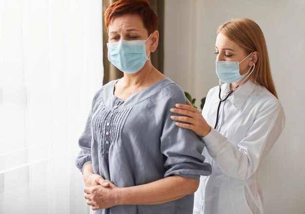 Paziente anziano con mascherina medica e medico femminile del centro di recupero covid con lo stetoscopio