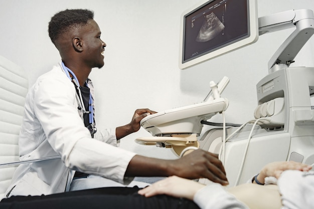 Paziente sul divano. Il dottore fa una diagnosi ecografica. Uomo in uniforme bianca.