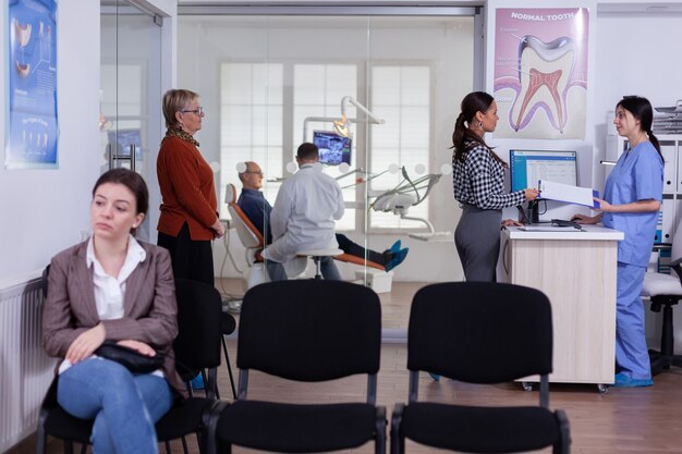 Pazienti in stomatologia in attesa in fila per compilare il modulo, medico che esamina un uomo anziano che discute di assistenza sanitaria