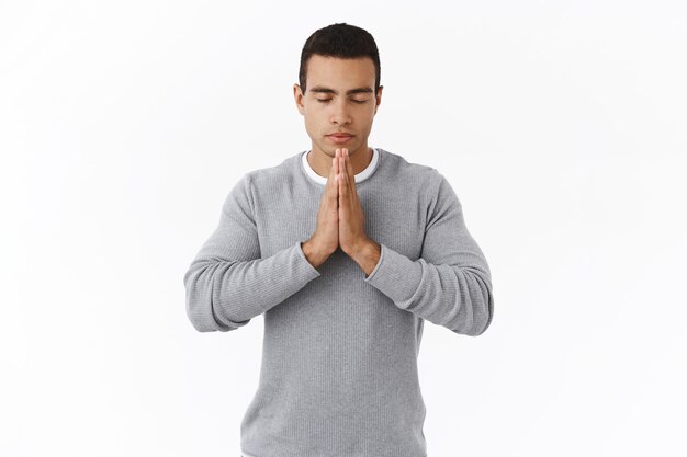 Pazienza e concetto di meditazione. Calmo determinato giovane ispanico in maglione, pregando Dio