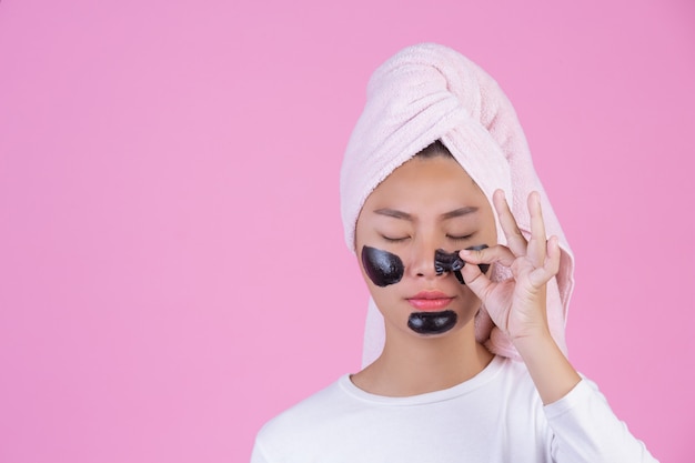 Peeling cosmetico di bellezza. Giovane femmina con la maschera nera staccata sul prodotto cosmetico della sbucciatura di cura di pelle della pelle sul viso su un rosa.
