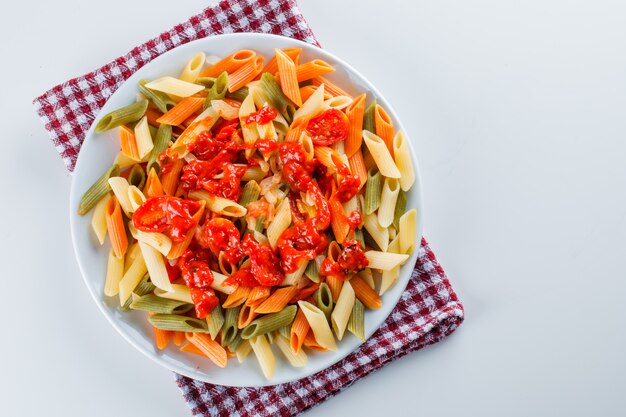 Penne al pomodoro, salsa in un piatto su bianco e asciugamano da cucina