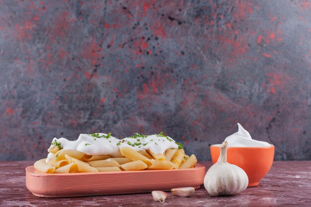 Penne con maionese e aglio fresco su un tavolo luminoso.