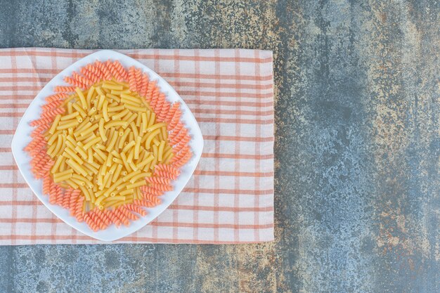 Penne e fusilli crudi nella ciotola sul tovagliolo, sui precedenti di marmo.