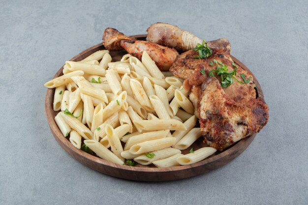 Penne e pollo alla griglia su piatto di legno.