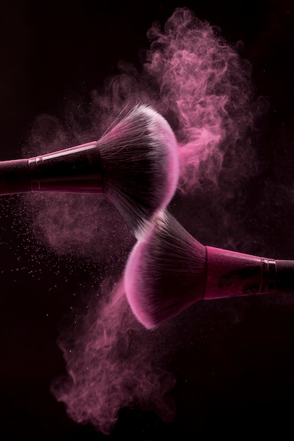 Pennelli cosmetici in nebbia di polvere rosa su sfondo scuro