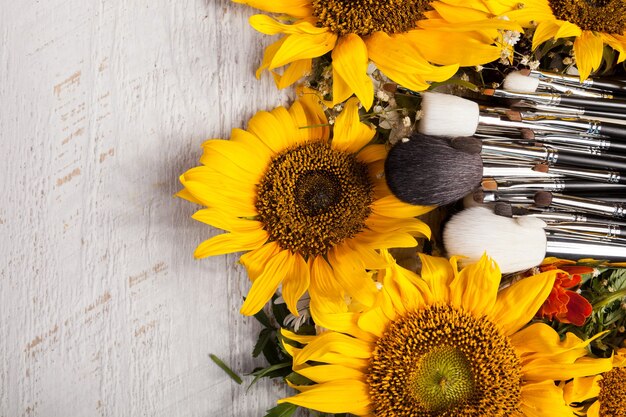 Pennelli per il trucco accanto a bellissimi fiori selvatici su fondo in legno