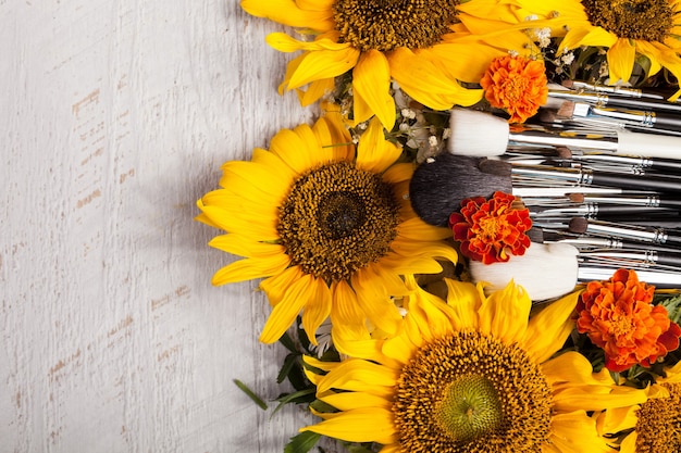 Pennelli per il trucco accanto a bellissimi fiori selvatici su fondo in legno