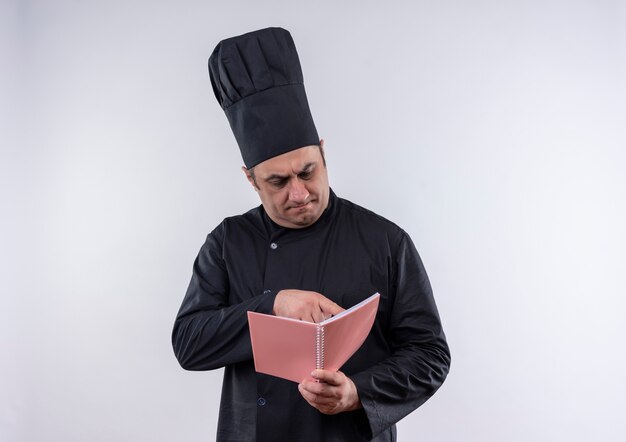 Pensando cuoco maschio di mezza età in uniforme da chef leggendo qualcosa sul taccuino in mano